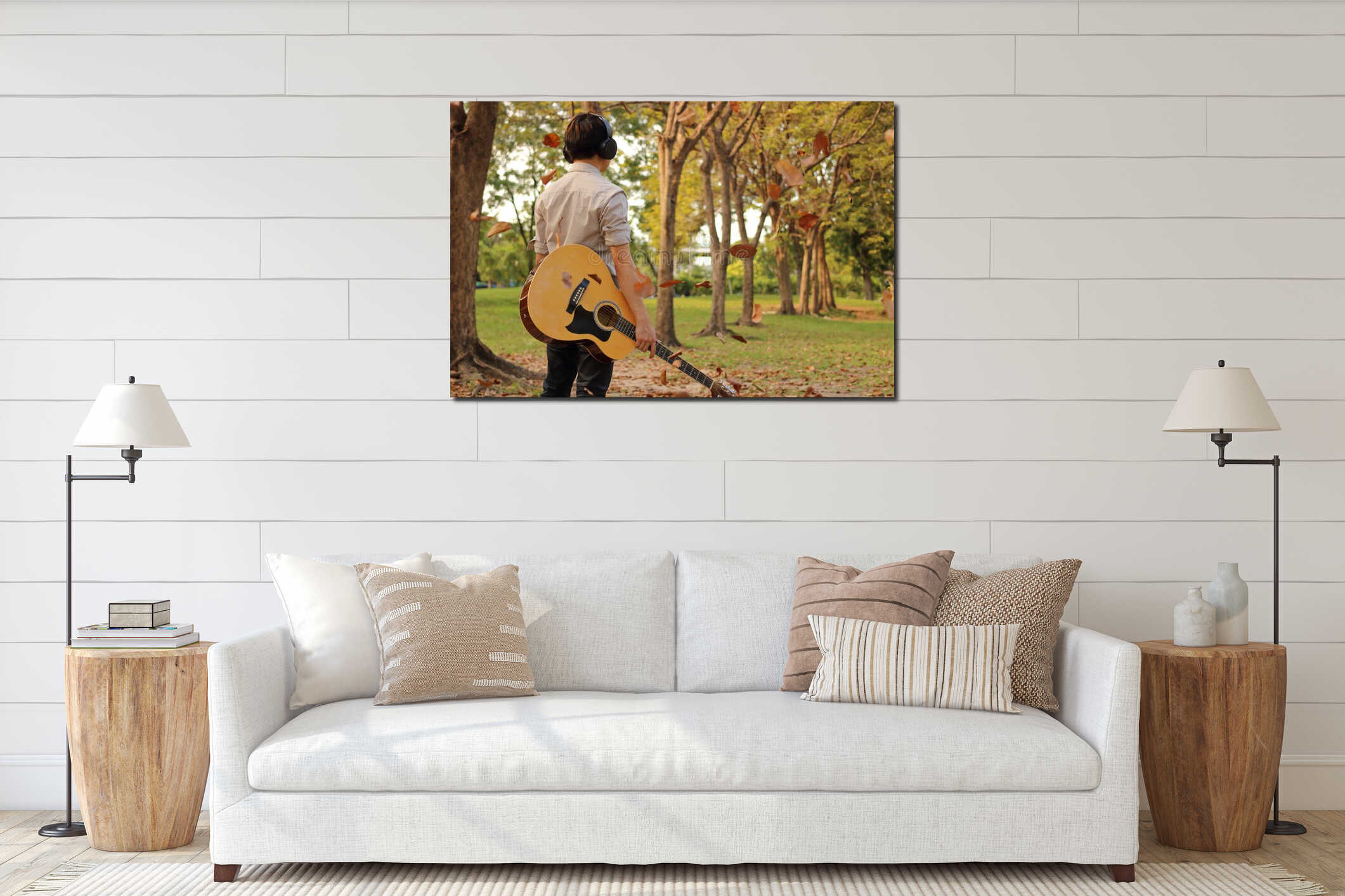 Rear view of portrait of handsome young man holding acoustic guitar with headphones against among falling leaves in the park outdo interior mockup