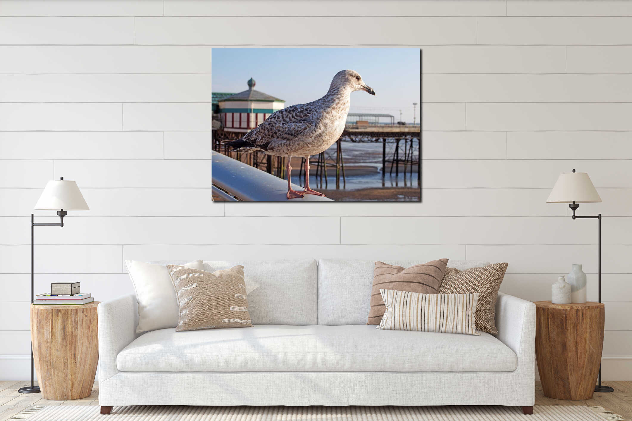 Close up of a juvenile herring gull stood on a railing with blackpool north pier in the background reflected in water on the beach interior mockup