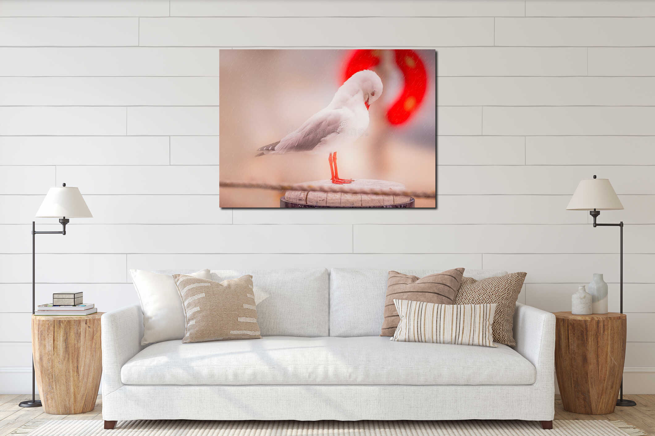 A seagull with red legs and a red beak bends his head to try and shelter from the rain. He is standing on a wooden post interior mockup