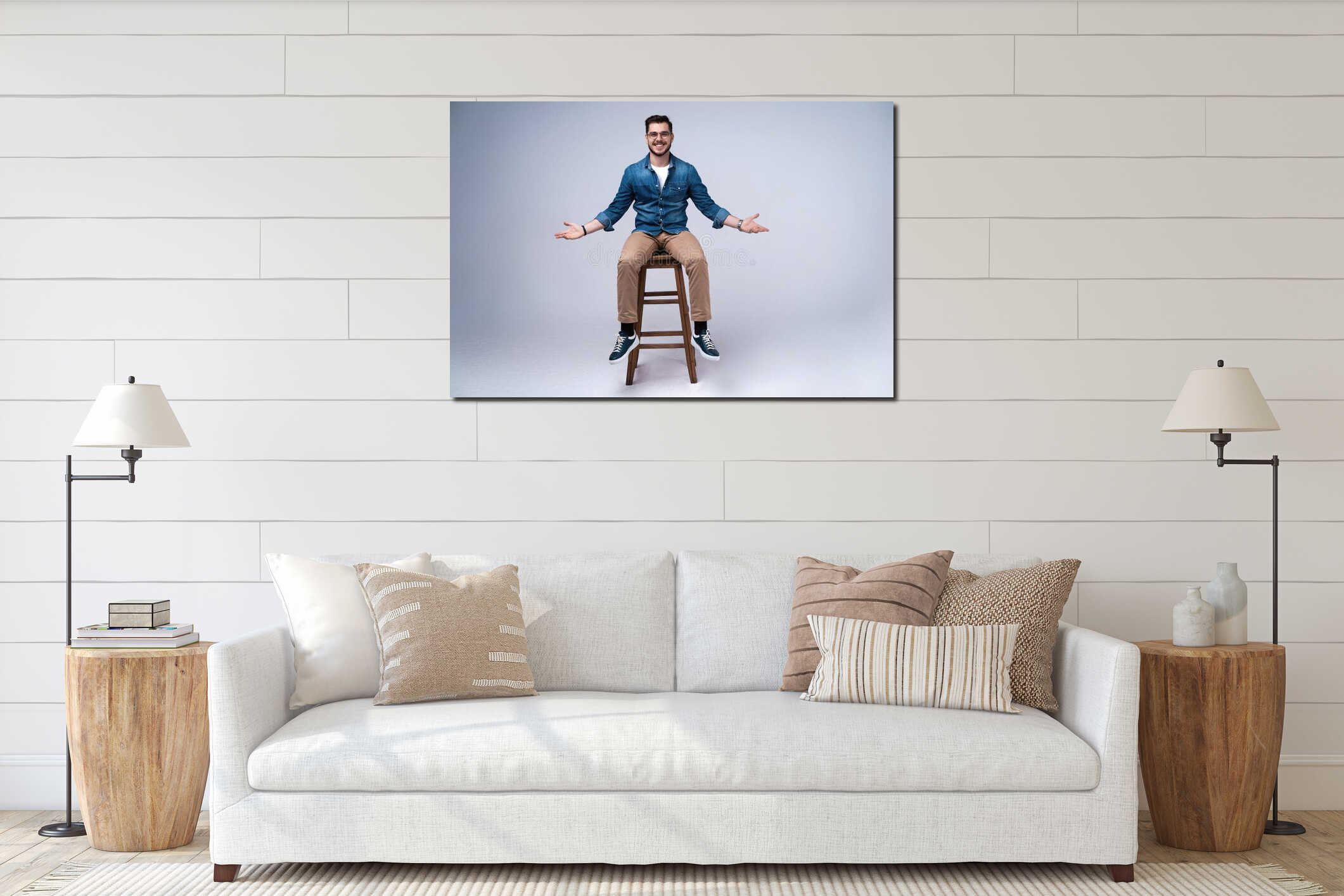Full length portrait of an attractive young man in jeans shirt sitting on the chair over grey background. interior mockup