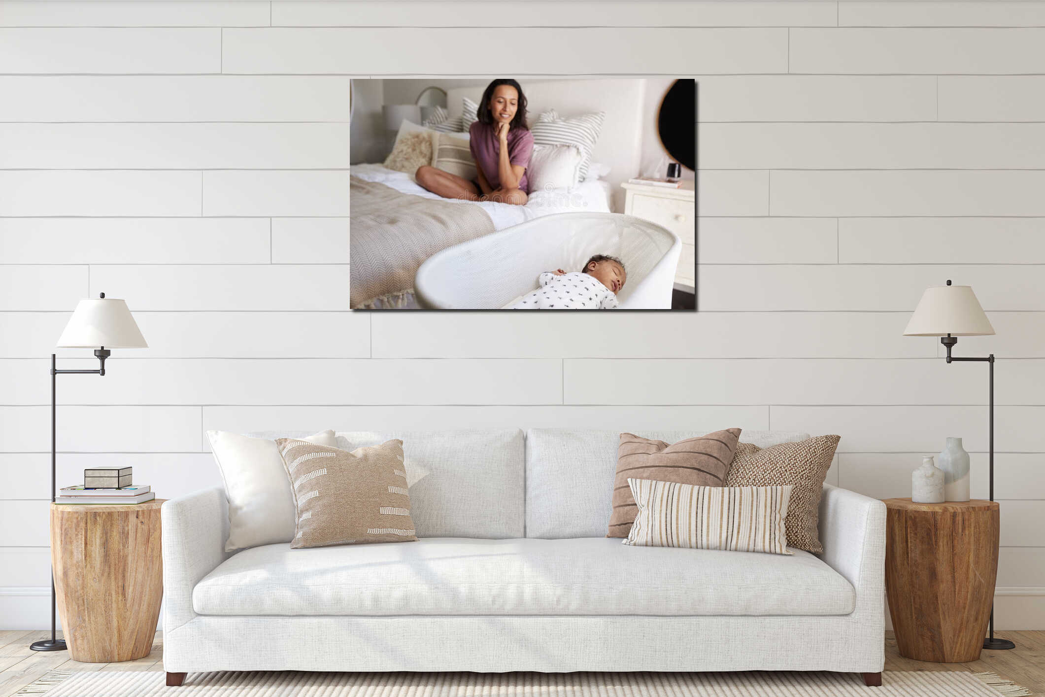 Young adult mother sitting cross legged on her bed looking down at her three month old baby sleeping in his cot, close up interior mockup