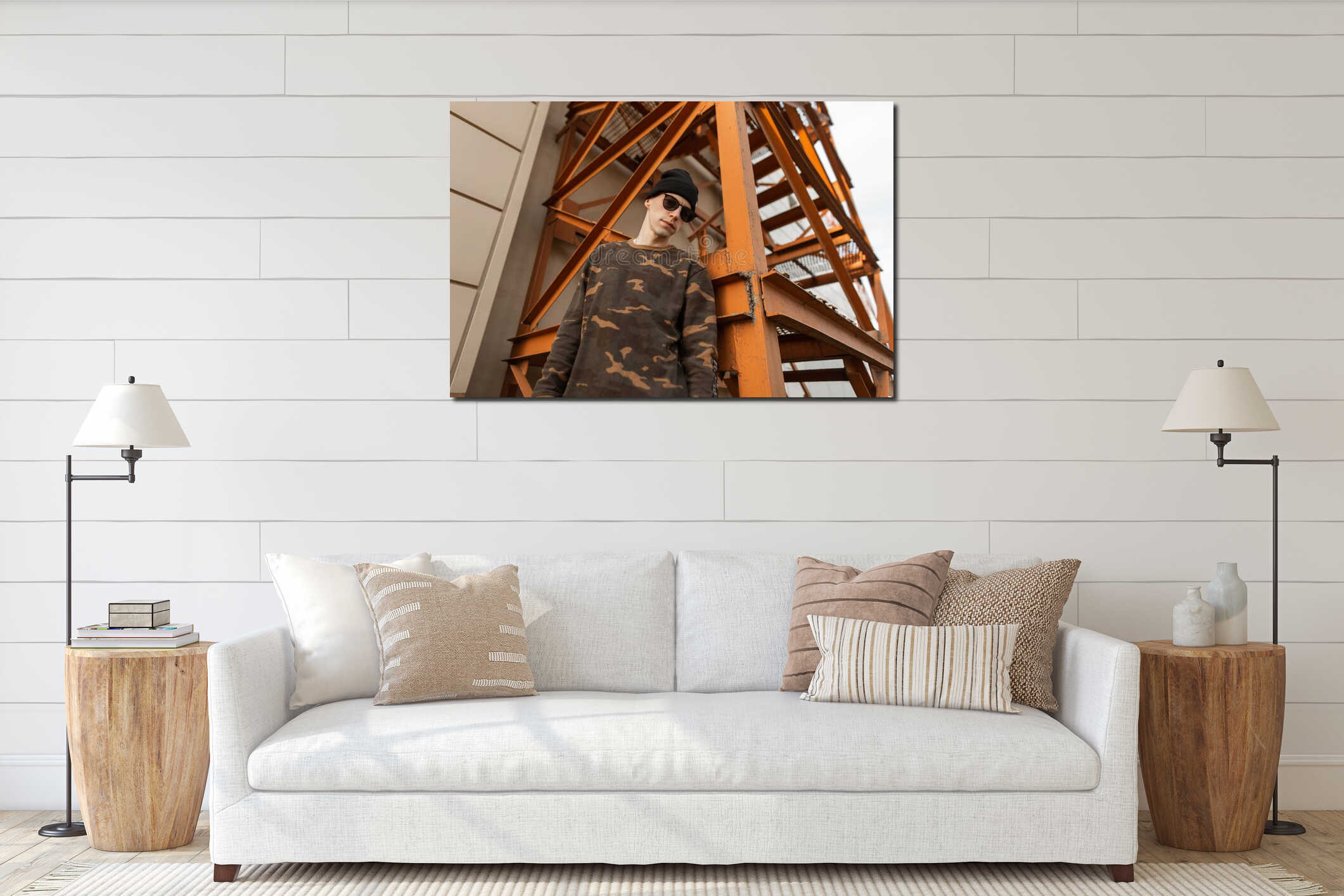 Young hipster man in a fashionable military shirt in a knitted hat in sunglasses stands near an orange vintage iron staircase interior mockup
