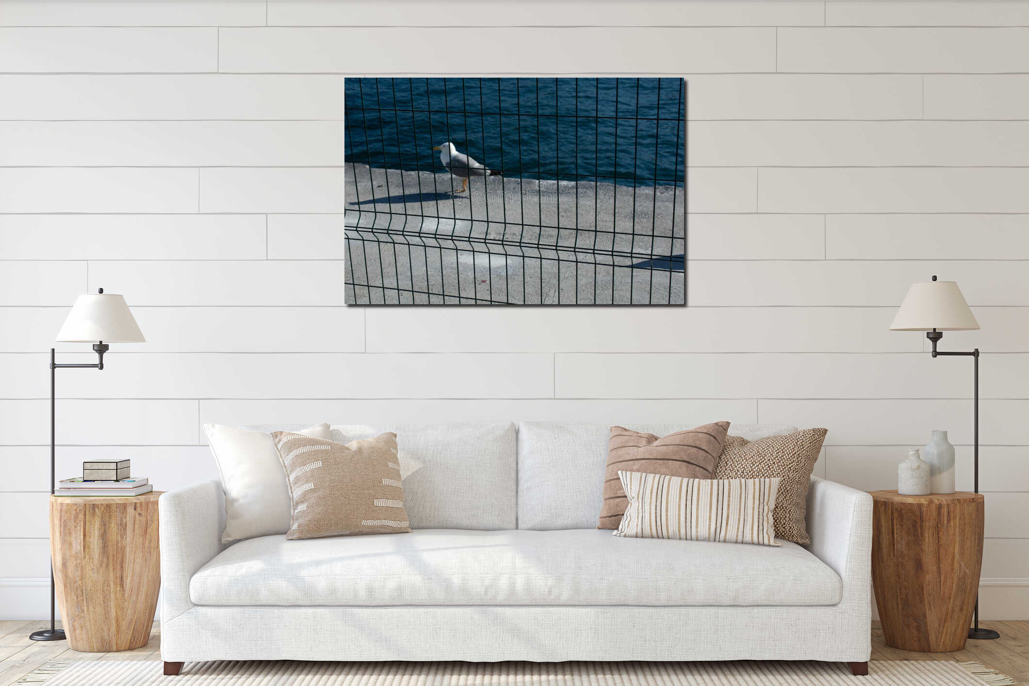 Closeup shot of a seagull standing on a stone border near the sea on an iron net foreground interior mockup
