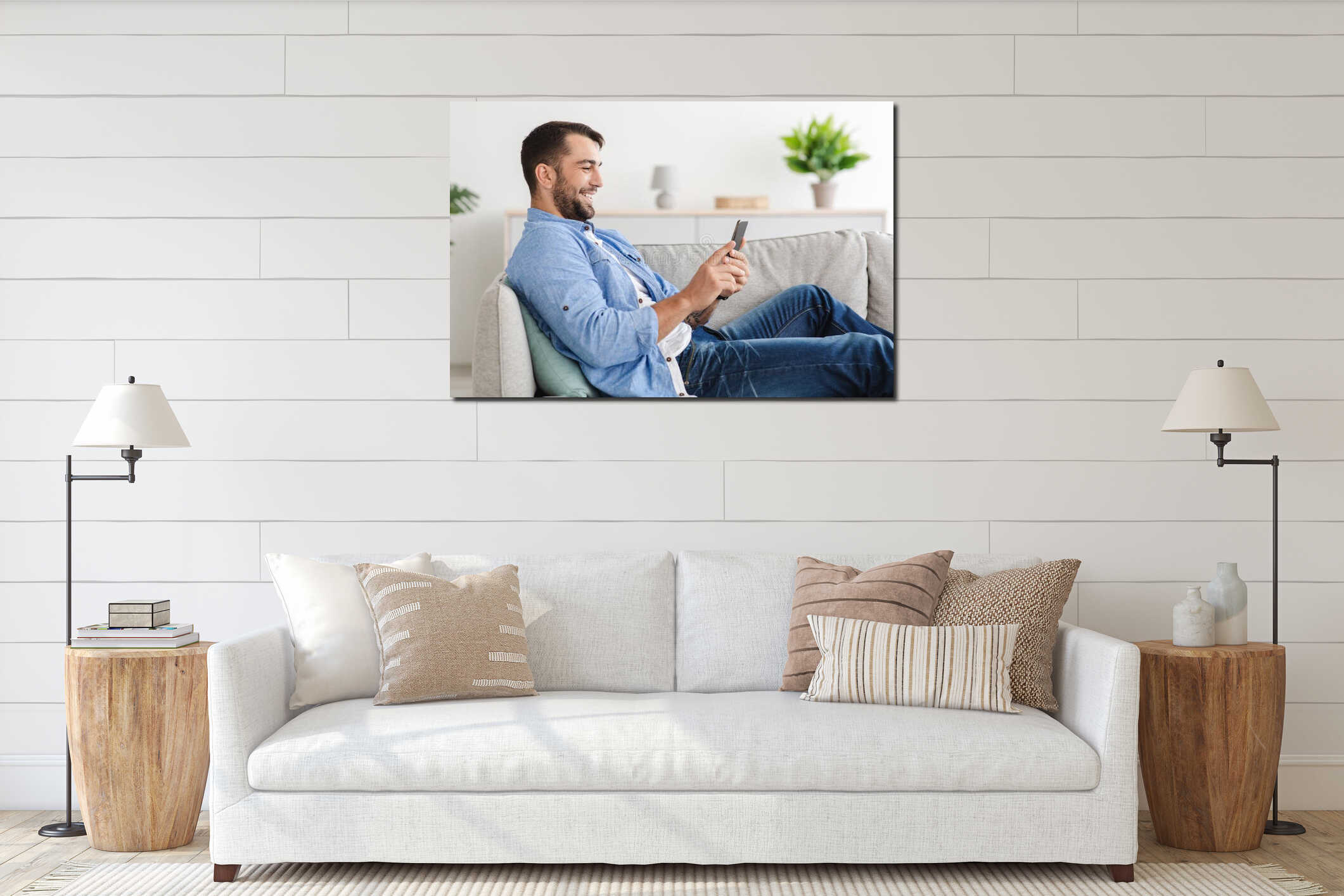 Cheerful adult european guy with beard sits on sofa chatting on phone in living room interior, side view interior mockup