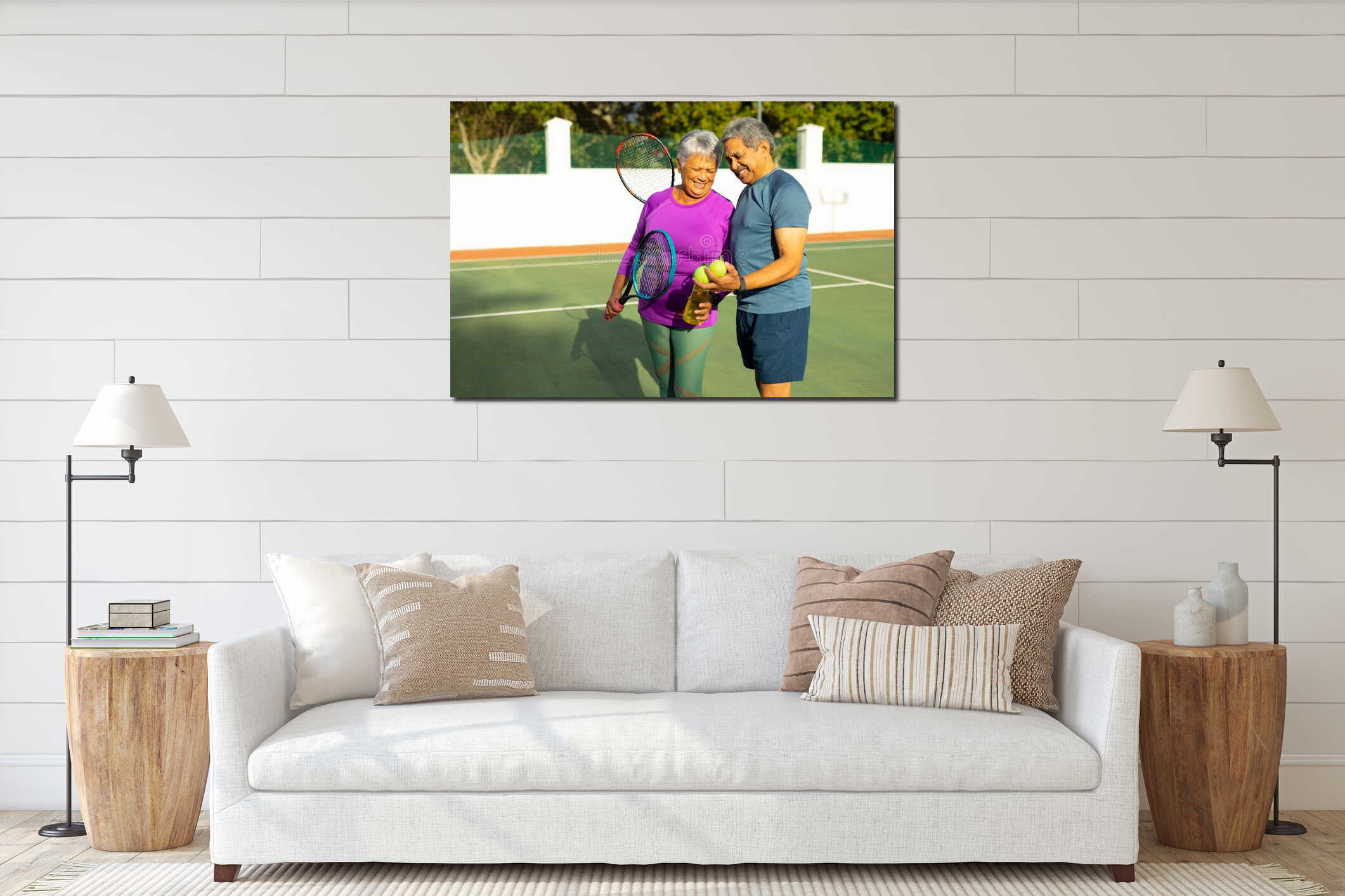 Happy biracial senior couple with tennis balls, rackets and water bottle standing in tennis court interior mockup