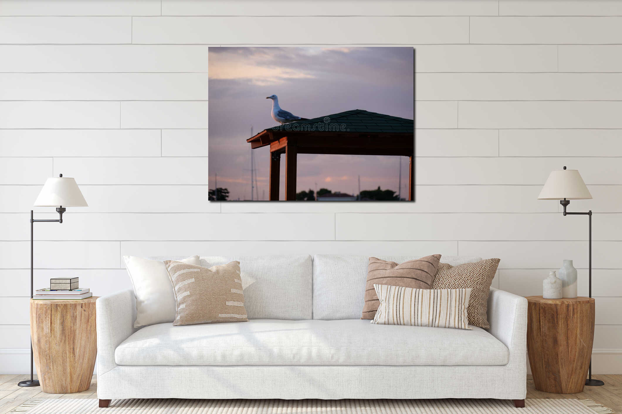 Side view of adorable seagull perched on the top of small roof on sunset sky background interior mockup