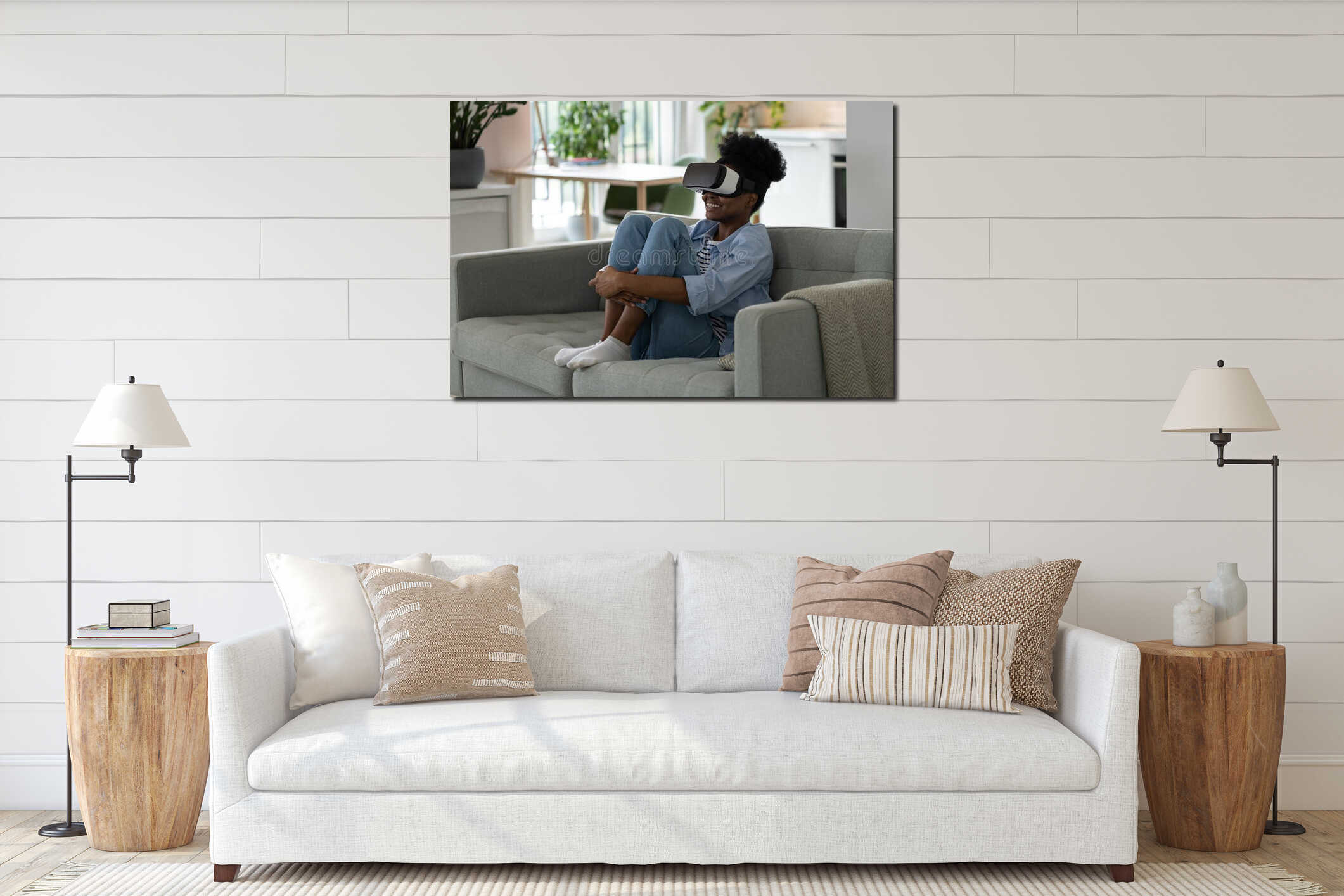 Young joyful African woman sitting on sofa in VR headset, watching immersive 3D video at home interior mockup