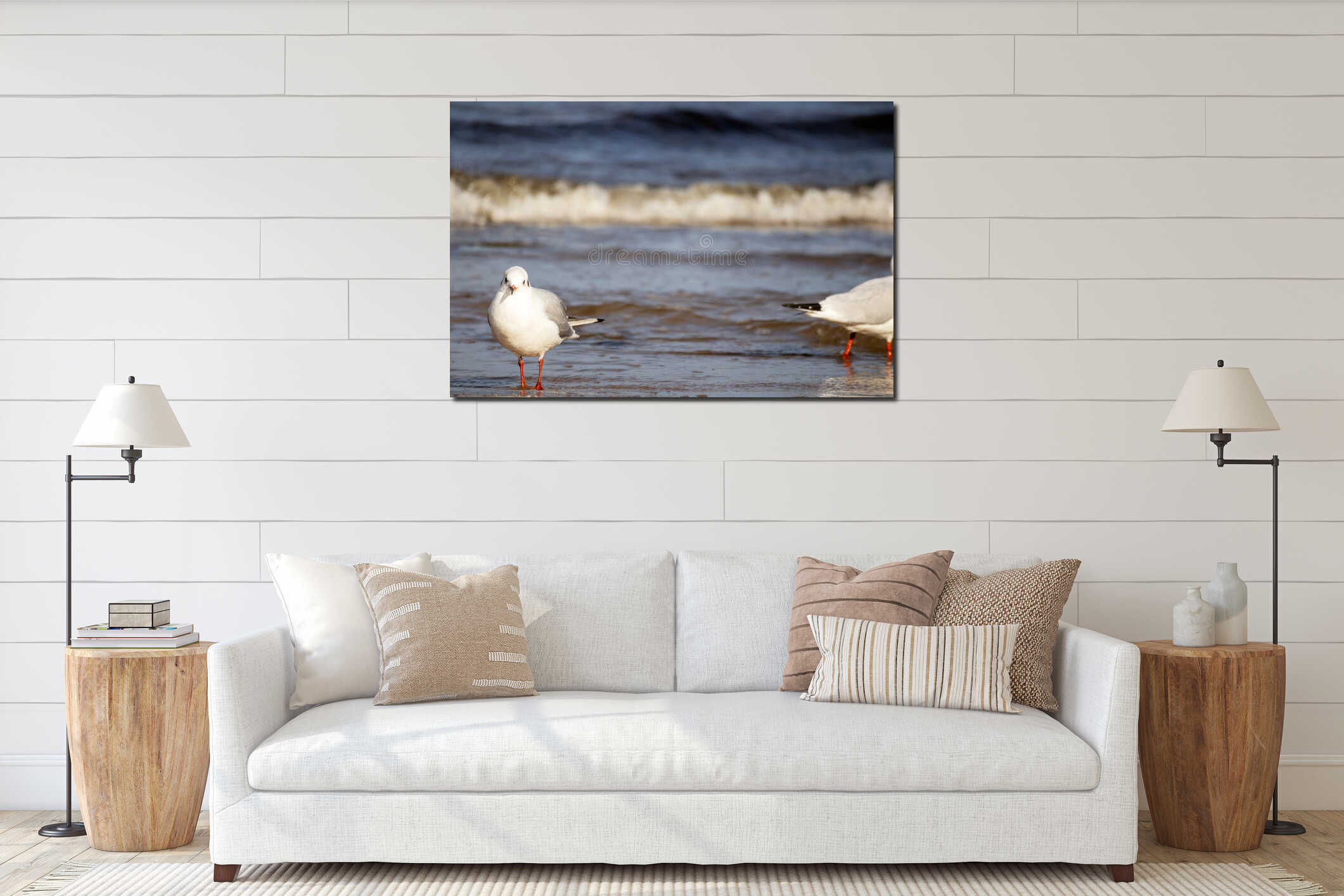 A white seagull with a red beak and red legs stands in the sea water with waves and brown sea sand on a sunny day interior mockup
