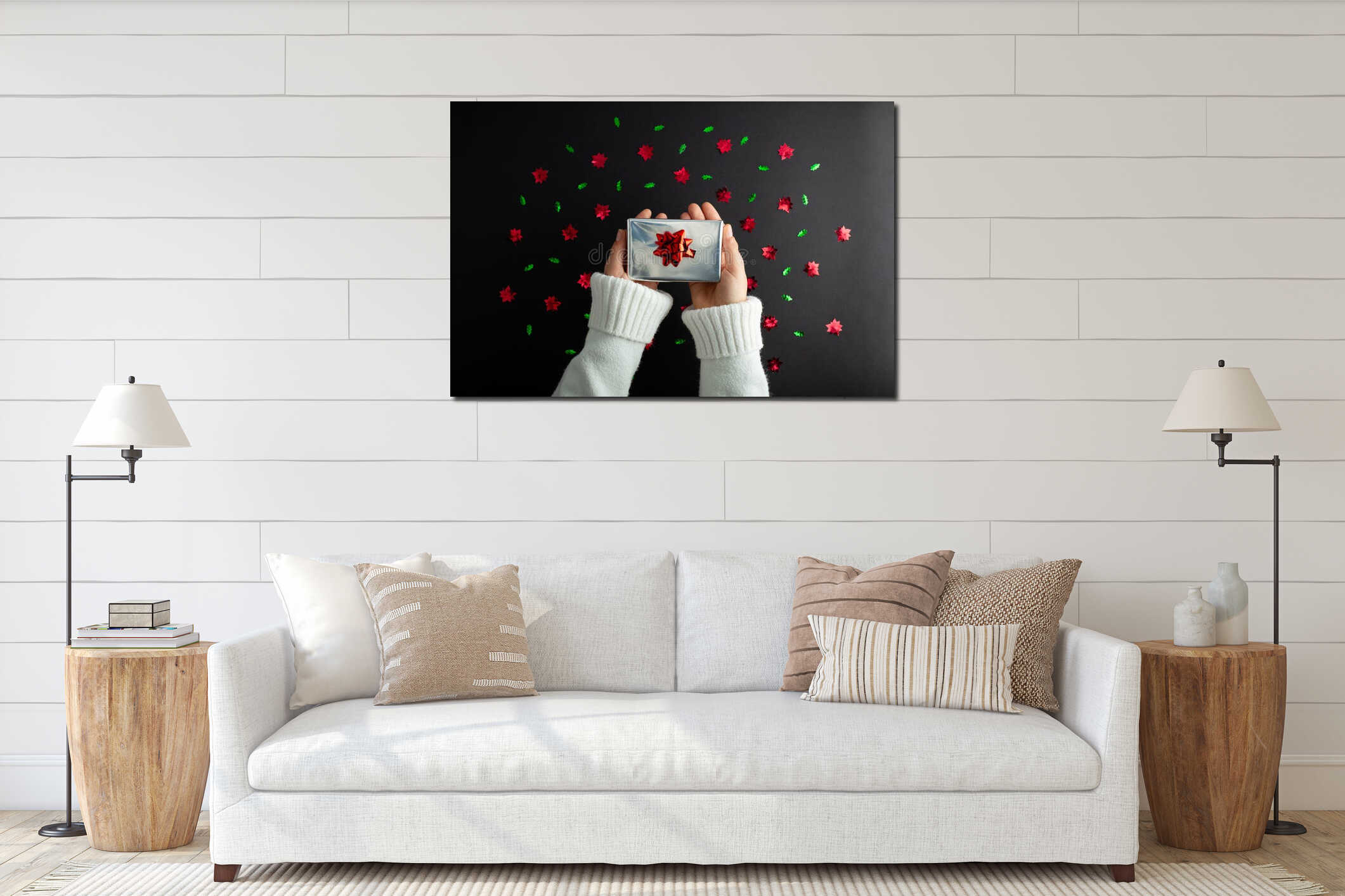 First person top view photo of hand holding silver giftbox with red satin ribbon bow over shiny red and green sequins on isolated interior mockup