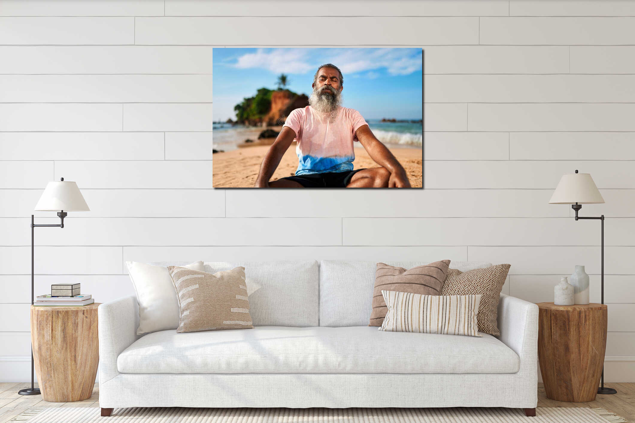 Elderly man with grey beard sits meditating on sandy beach. Serene ocean, blue sky, rocky island in background interior mockup
