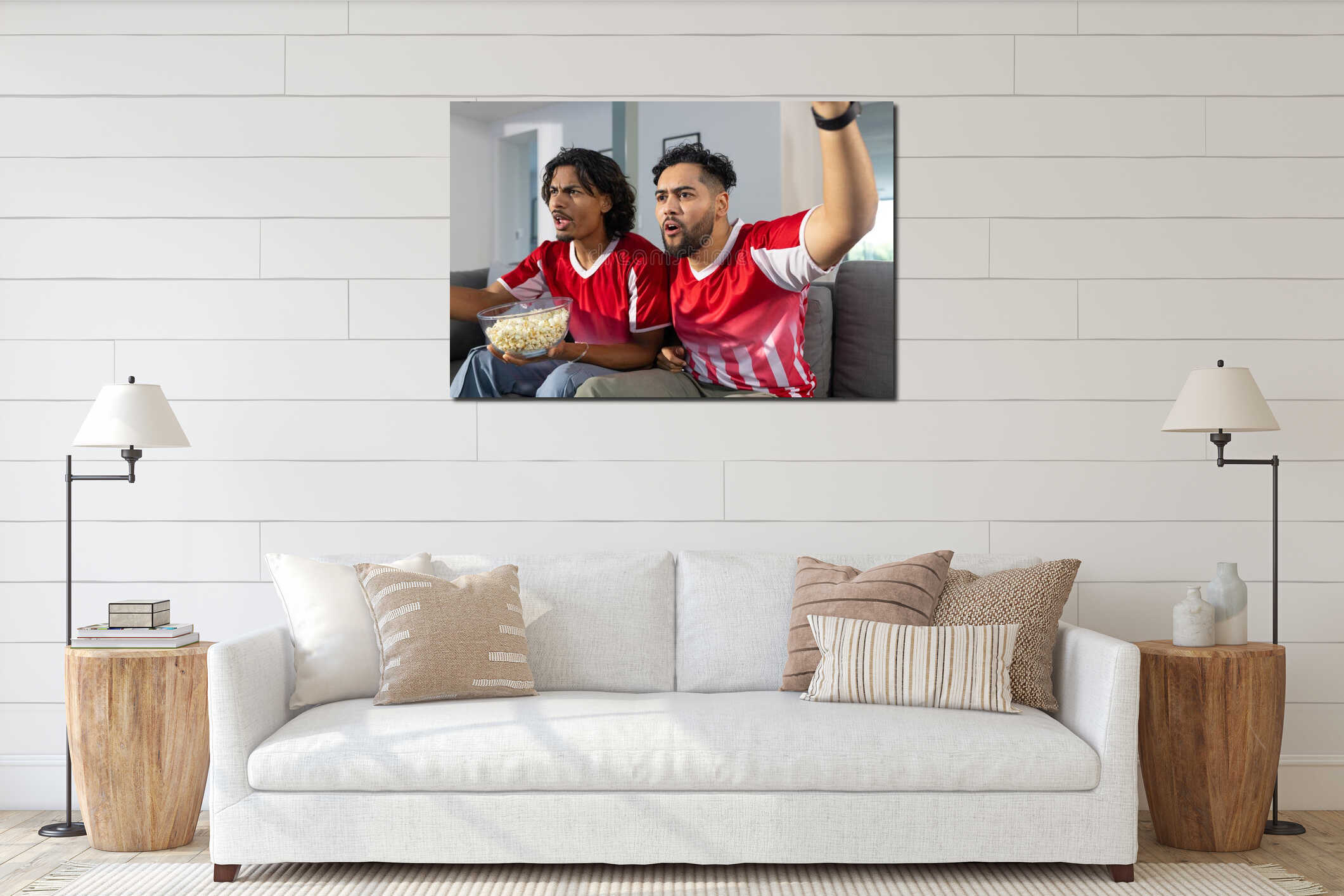 Male friends wearing red jerseys cheering on gray sofa in living room with bowl of popcorn interior mockup