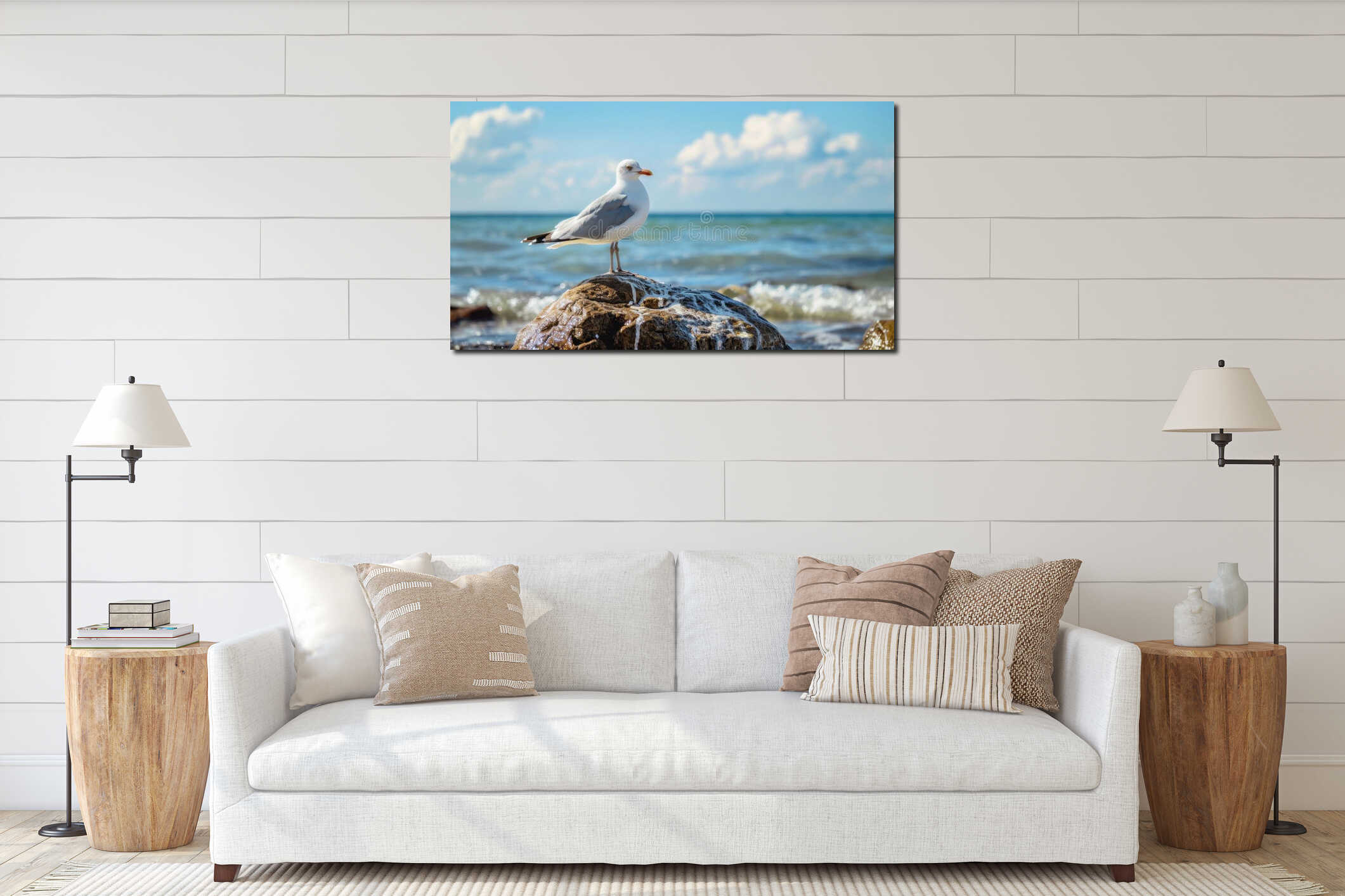 A seagull stands on a rock by the ocean. The water is blue with gentle waves. The sky is partly interior mockup
