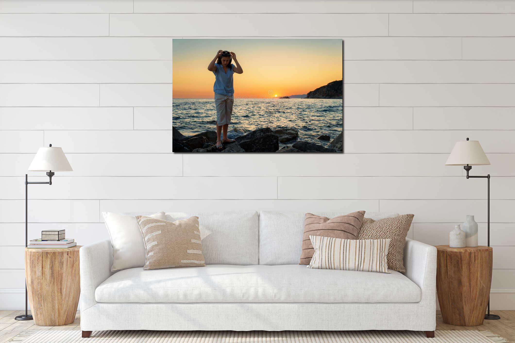 Young woman on a rocky beach at sunset, adjusting her sunglasses and looking down, peaceful summer evening atmosphere interior mockup